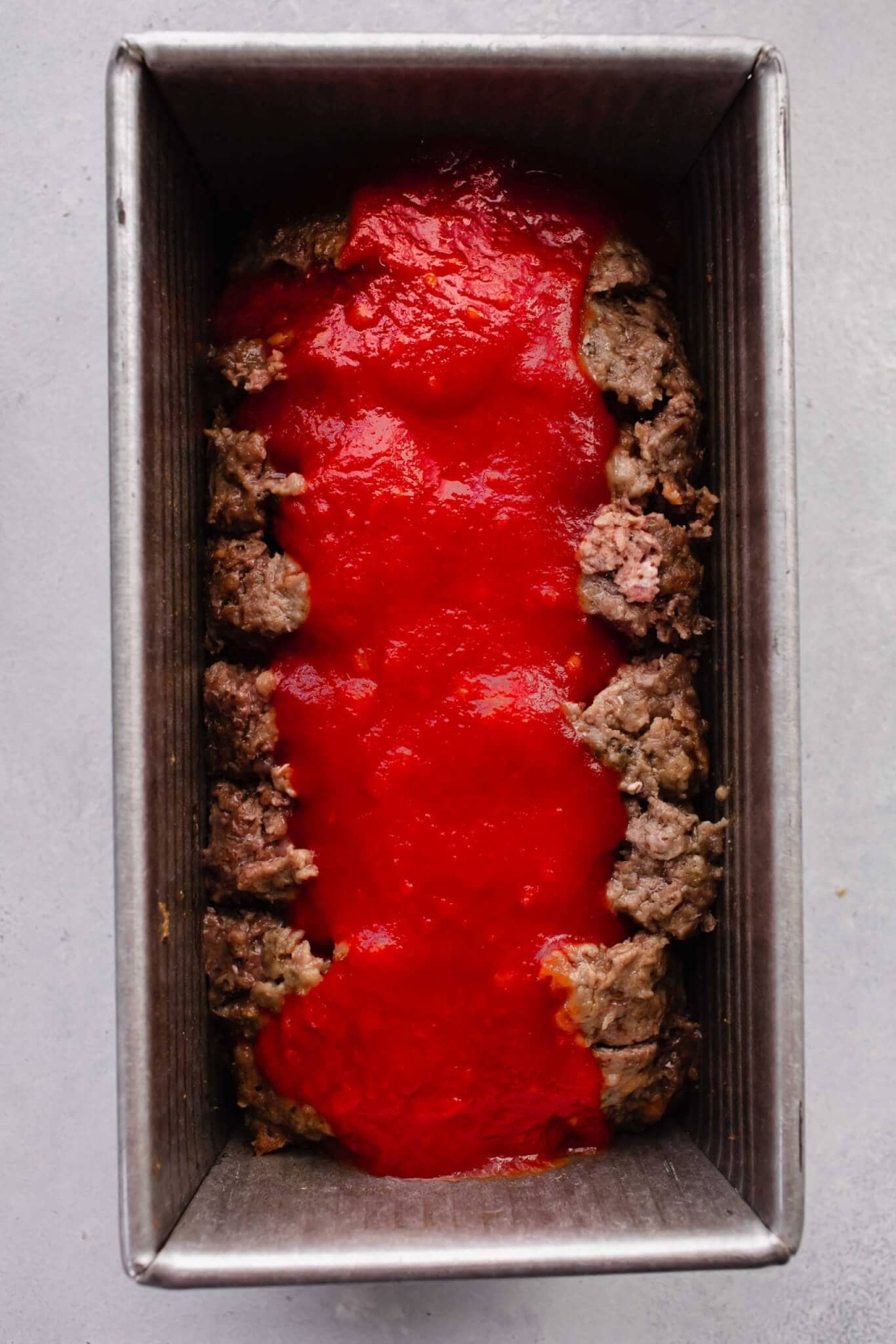 Half baked meatloaf after slicing and drizzling on tomato sauce.
