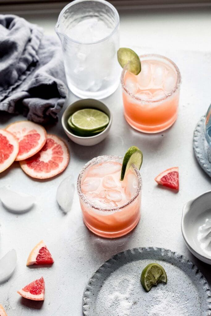 Grapefruit margaritas on counter with plate of salt and shaker. 