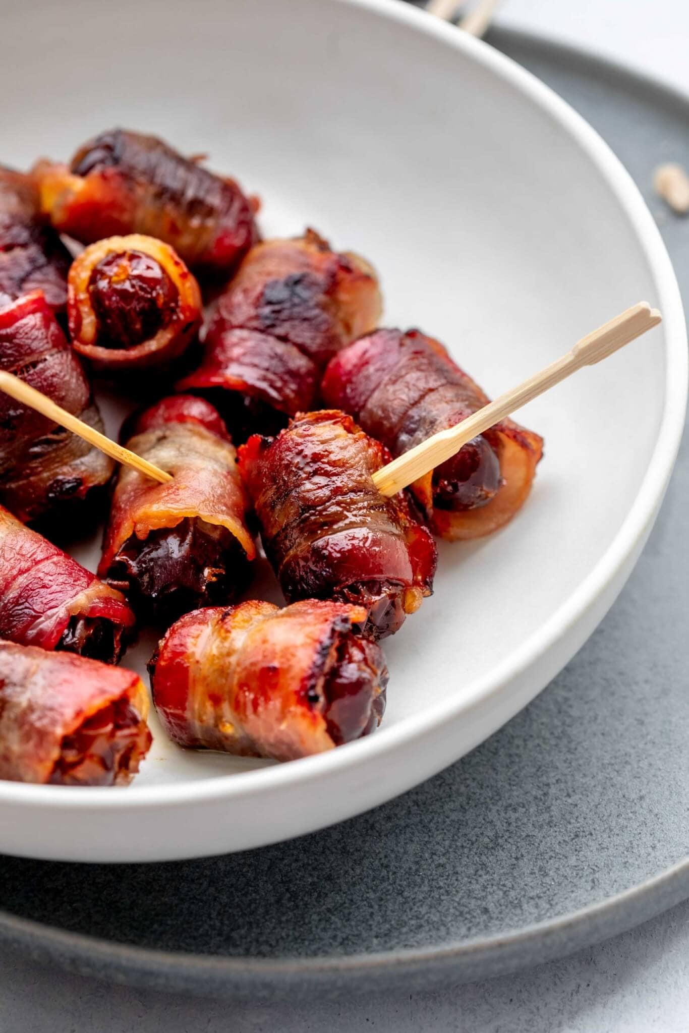 Side view of bowl of cooked bacon wrapped dates.