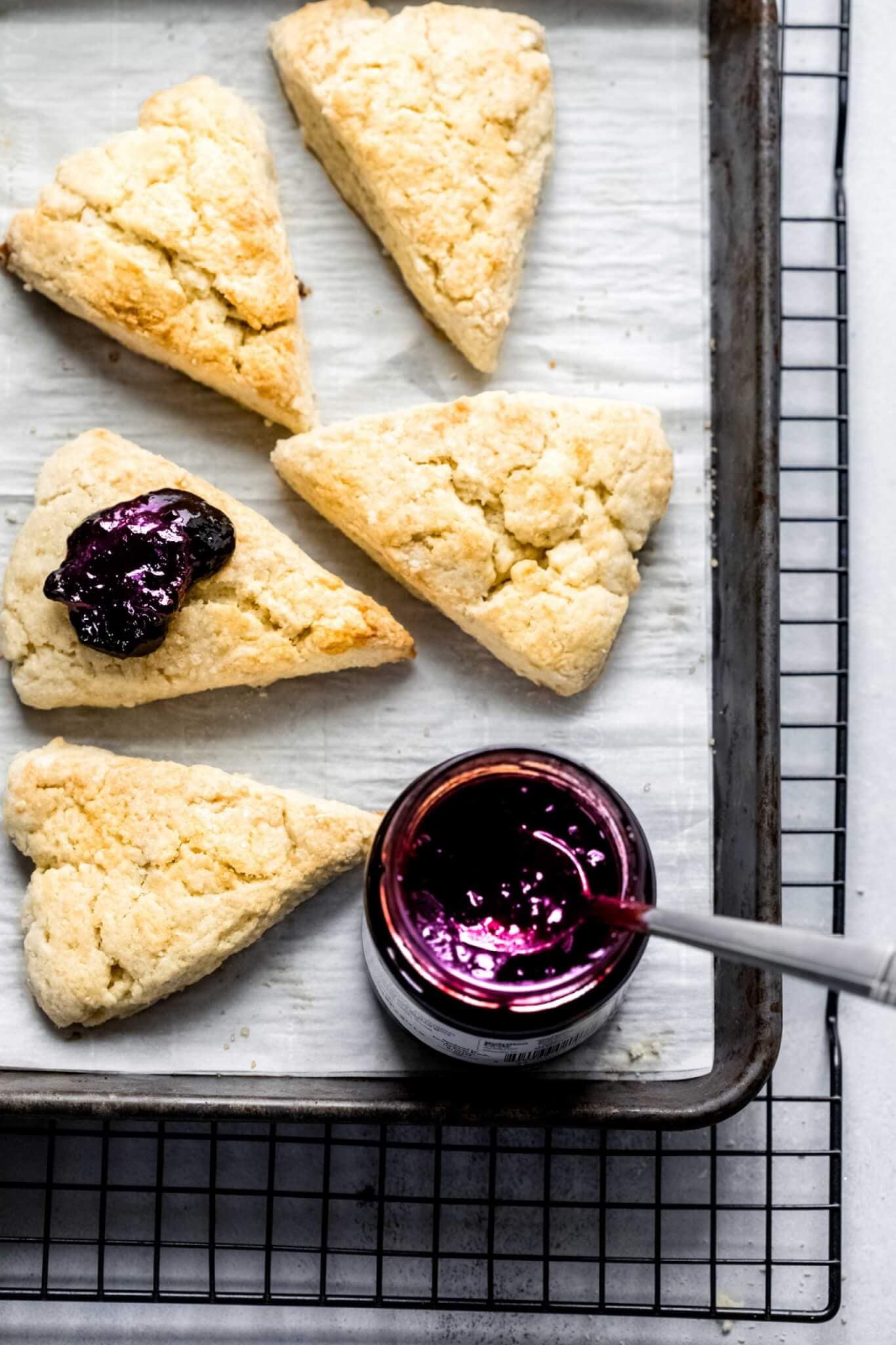 Cream scones on baking sheet next to jar of blackberry jam.