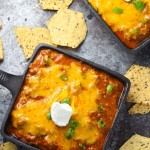Take your snacking to the next level with this Cheesy Enchilada Dip. Beans are layered with ground beef and enchilada sauce, and topped with lots of melty cheese, green onions and a dollop of sour cream. | platingsandpairings.com
