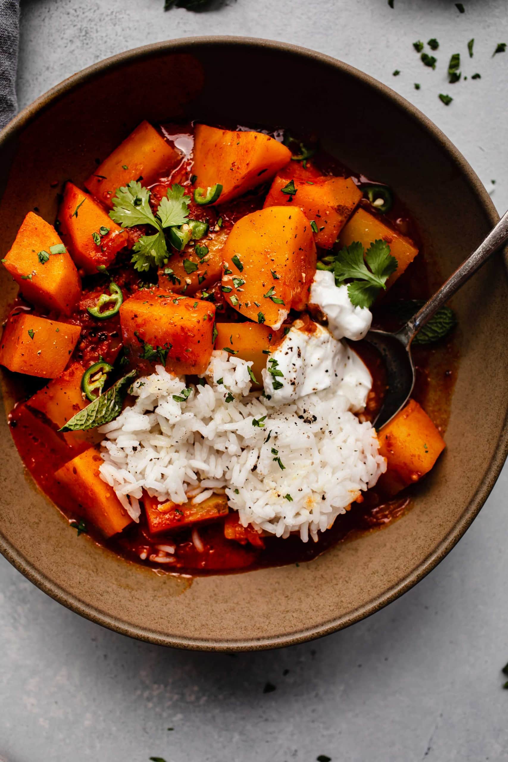 Potato vindaloo in brown bowl with greek yogurt and rice.