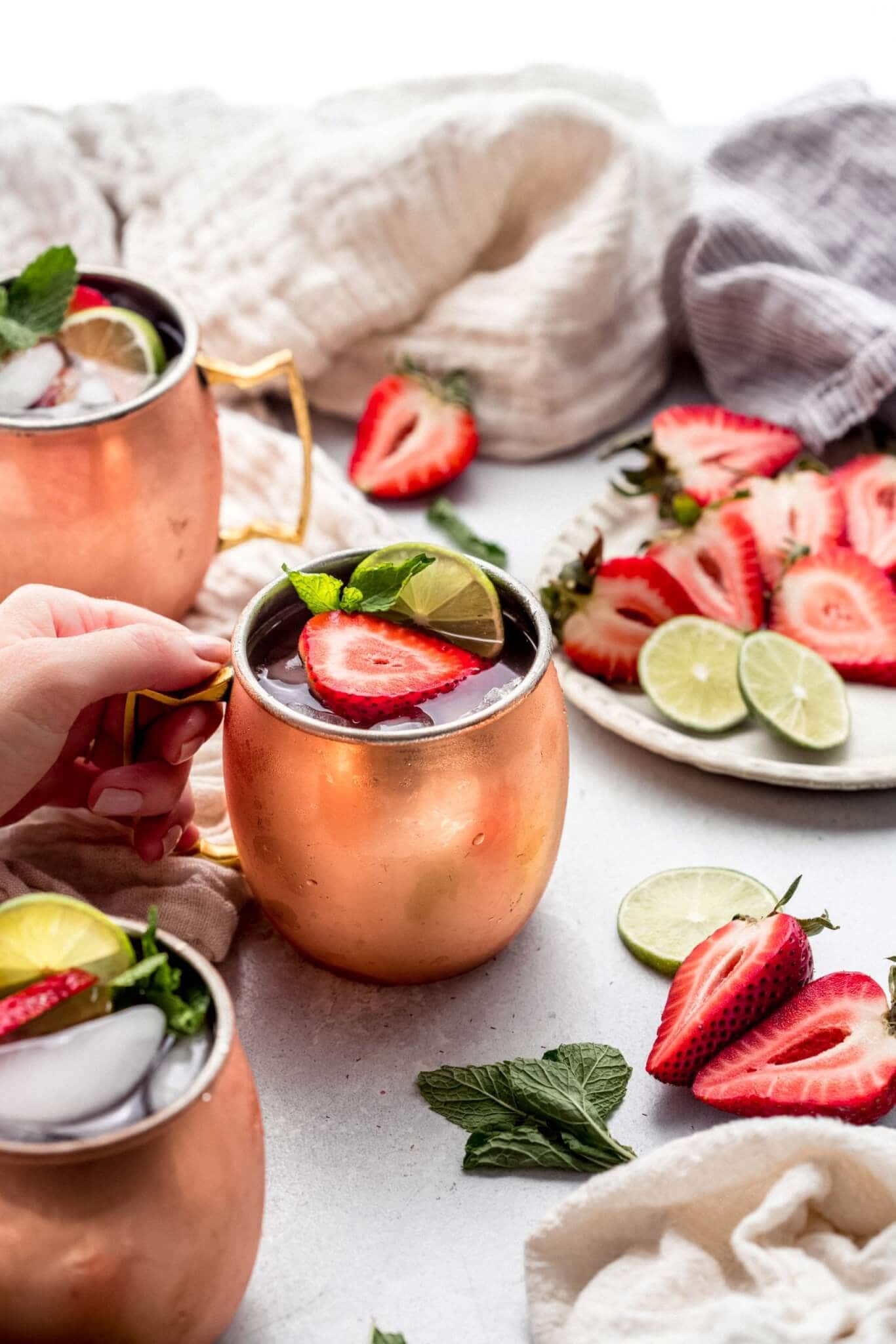 Hand holding copper mug filled with strawberry moscow mule cocktail.