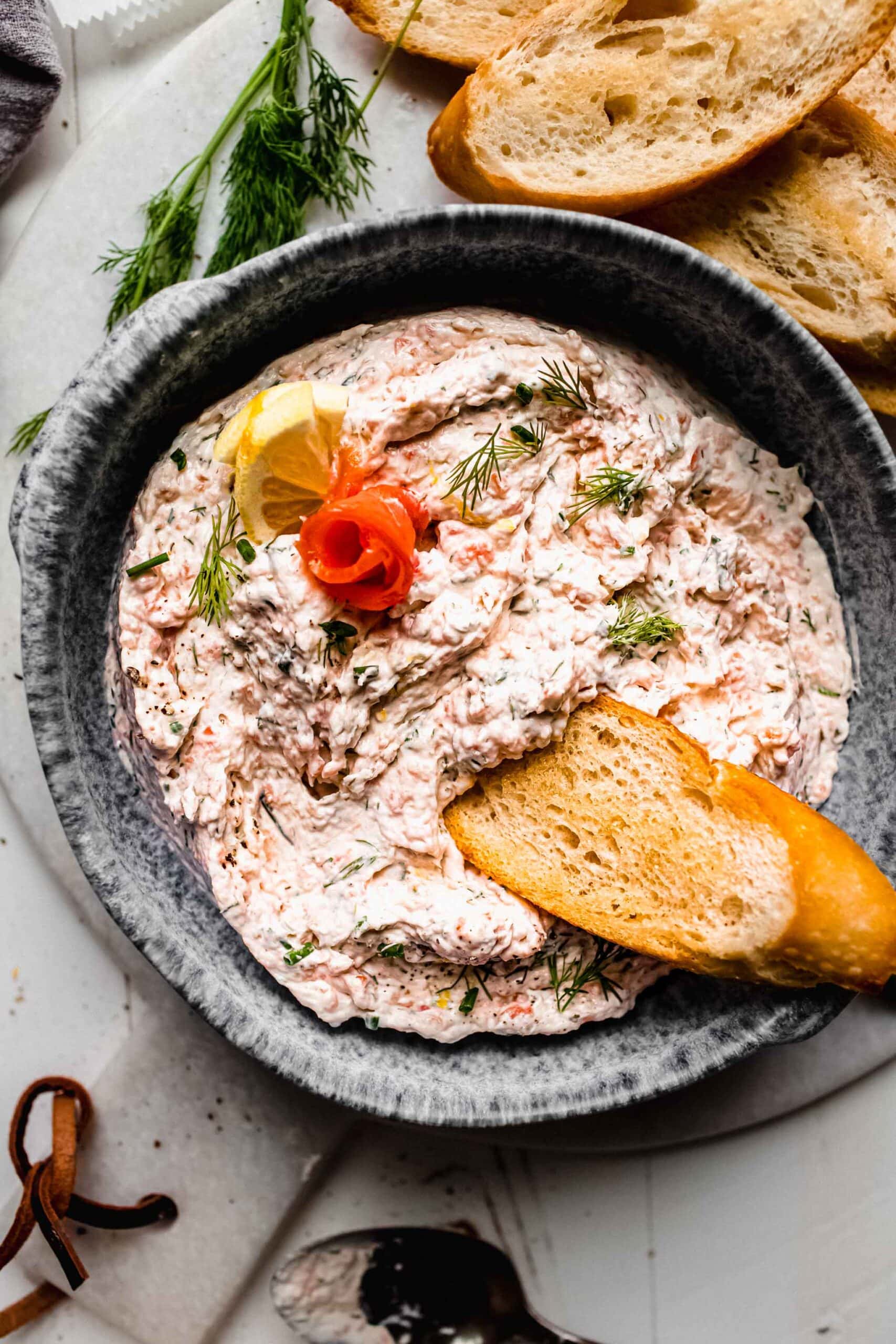 Bowl of smoked salmon dip with piece of crostini dipped into it.