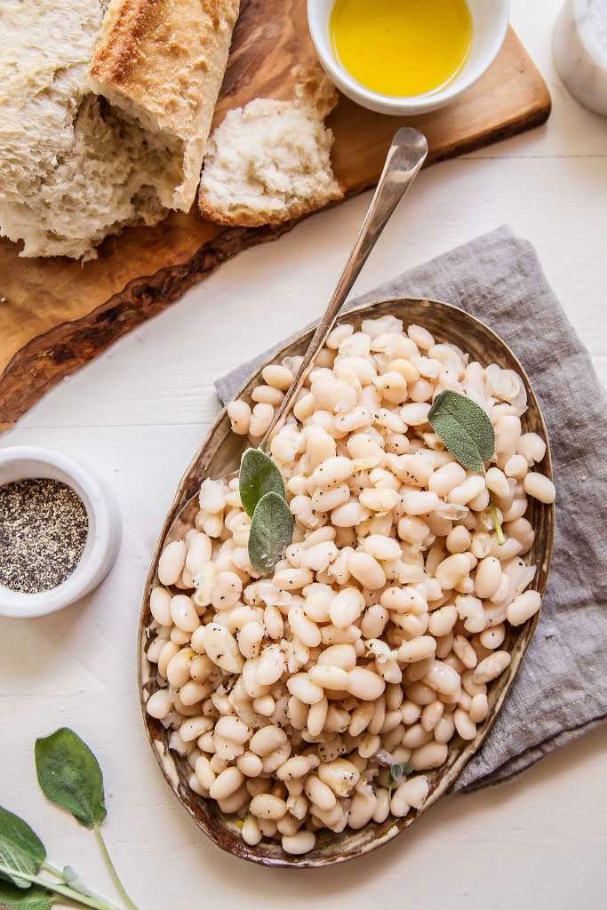 Italian white beans with sage next to loaf of bread with olive oil