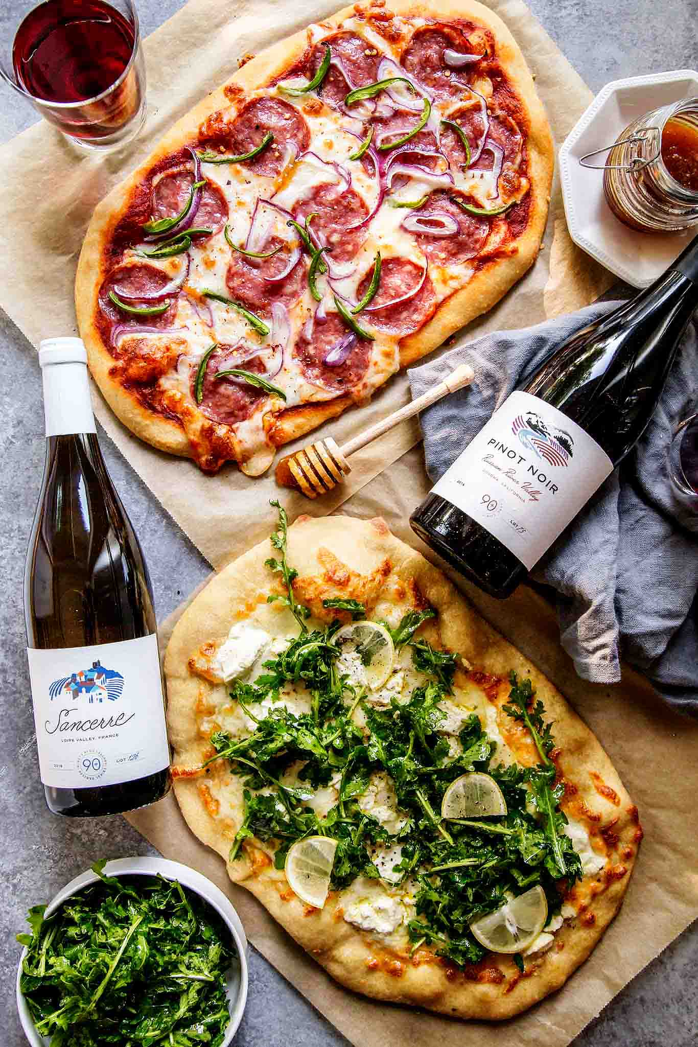 Learn how to host a wine & pizza party at home with these two simple pizza recipes. One features salami, jalapeno & honey and the other is a white pizza topped with goat cheese & arugula salad.