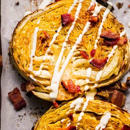 Close up of roasted cabbage steaks topped with bacon and drizzled with cream sauce.
