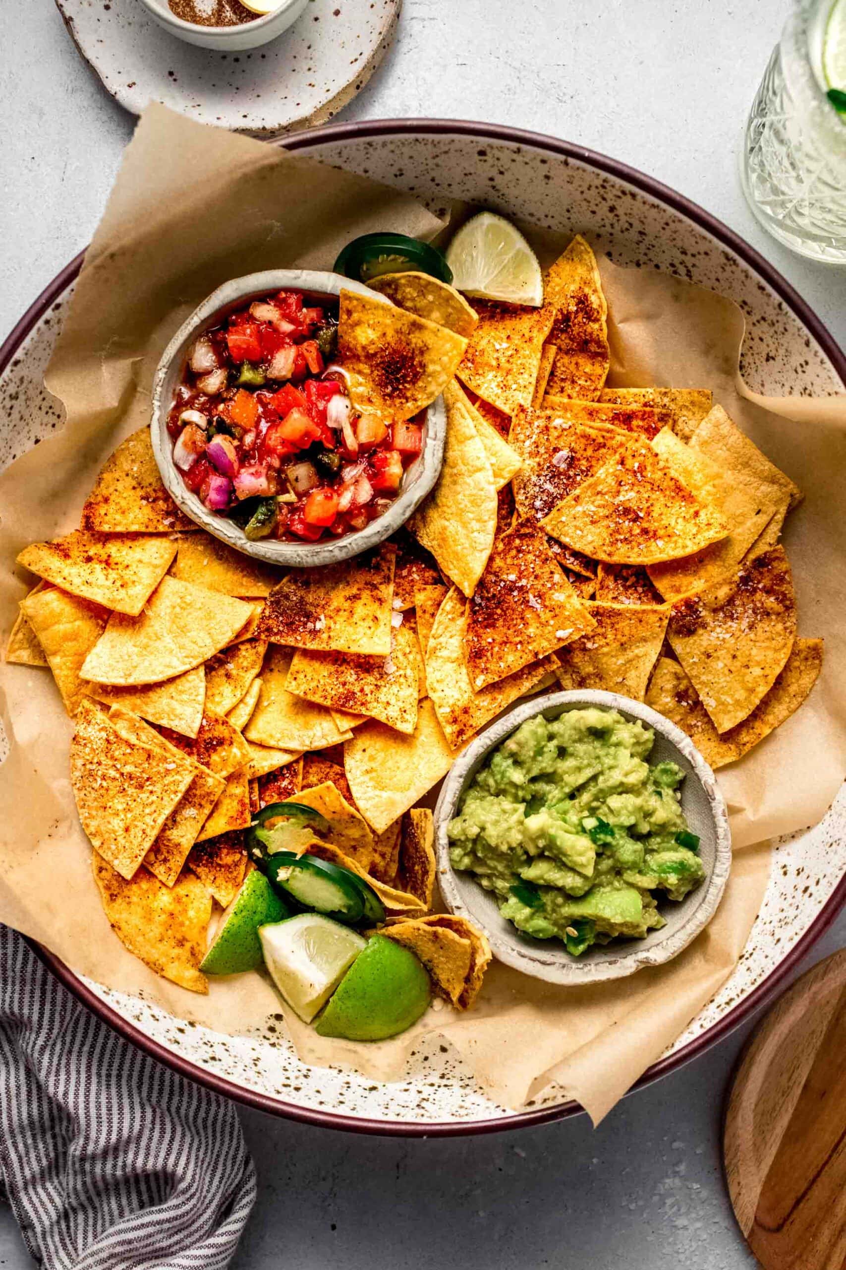 Baked tortilla chips in basket with guacamole and salsa.