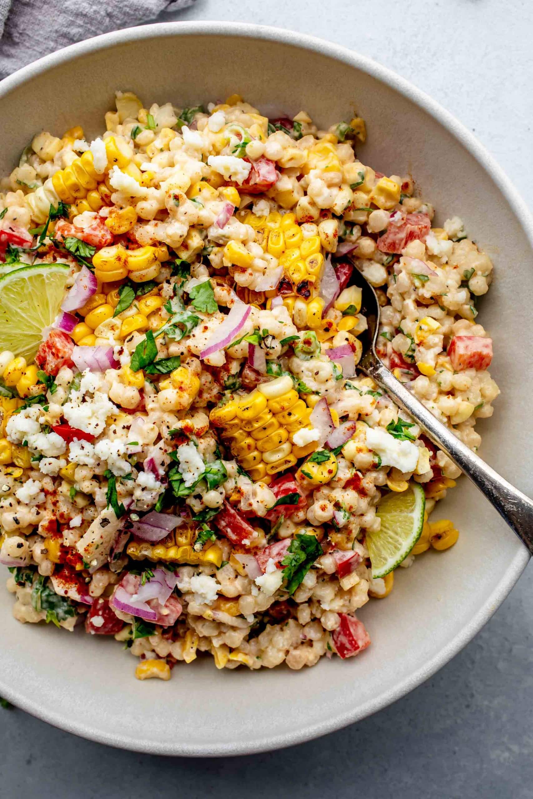 Street corn salad in white bowl with serving spoon.