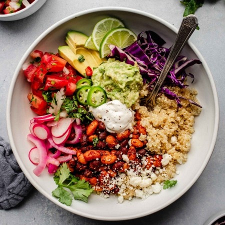 Quinoa topped with burrito bowl ingredients in white bowl with spoon.