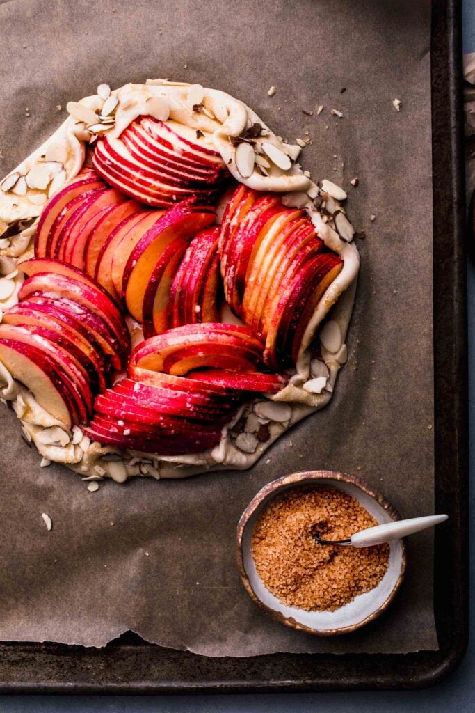 Apple galette on baking sheet next to coarse brown sugar.