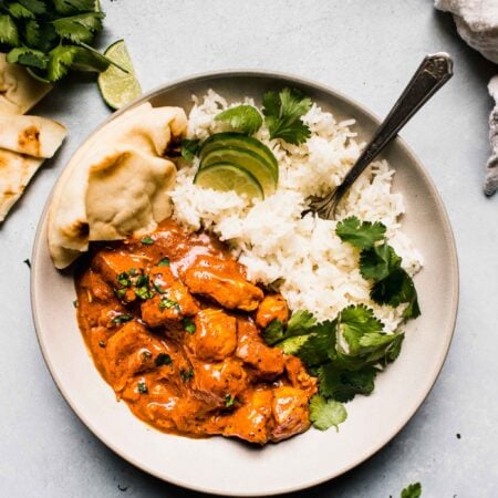 Overhead shot of instant pot butter chicken in white bowl with rice and naan.