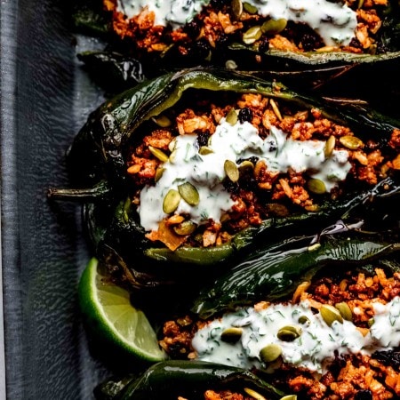 Overhead shot of stuffed poblanos arranged in baking dish drizzled with lime crema.