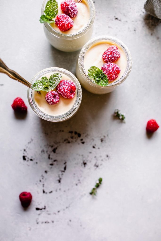 Overhead shot of three jars of ricotta mousse topped with raspberries, mint and powdered sugar.