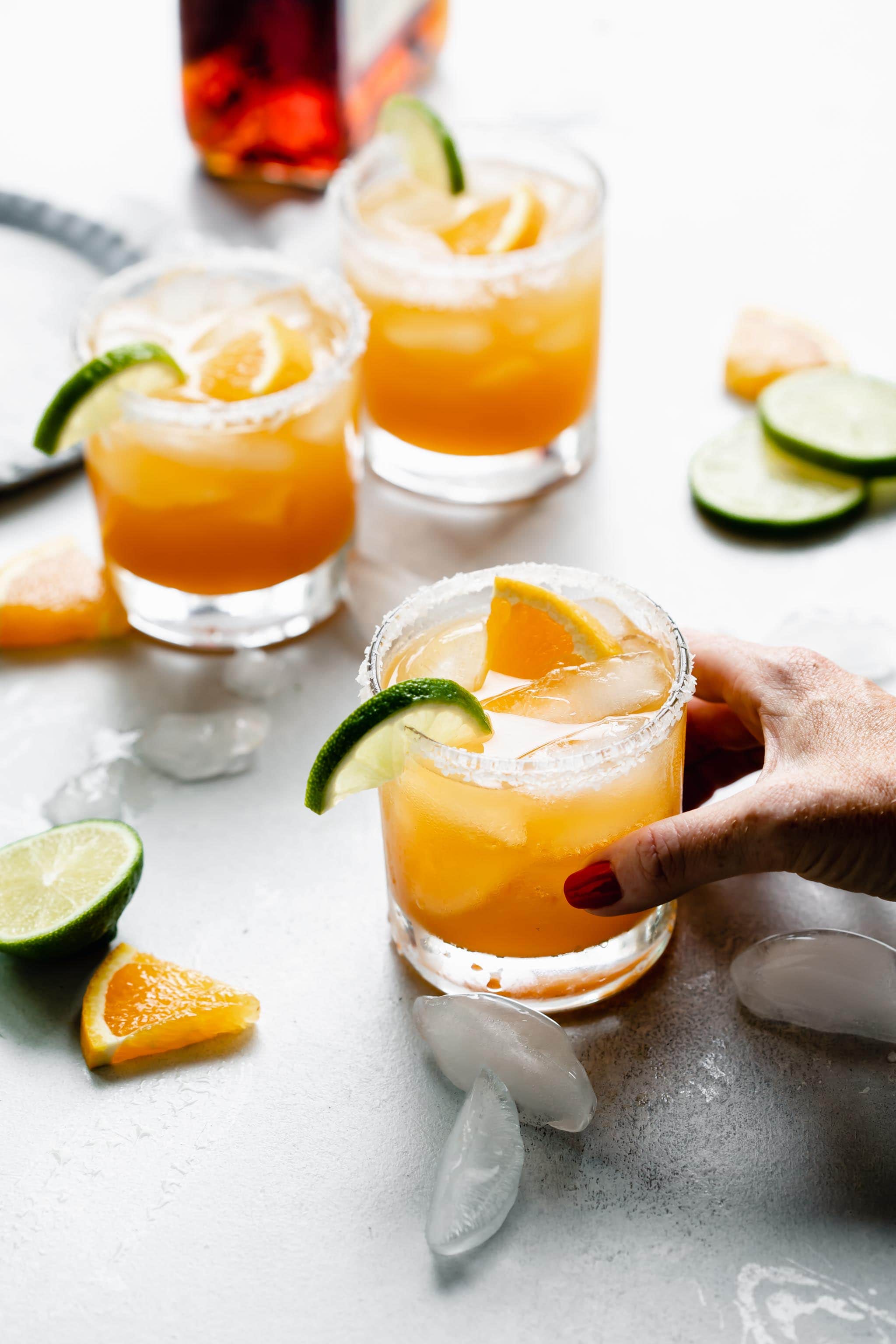 Hand holding glass of Italian Margarita rimmed with salt and garnished with orange and lime slices.
