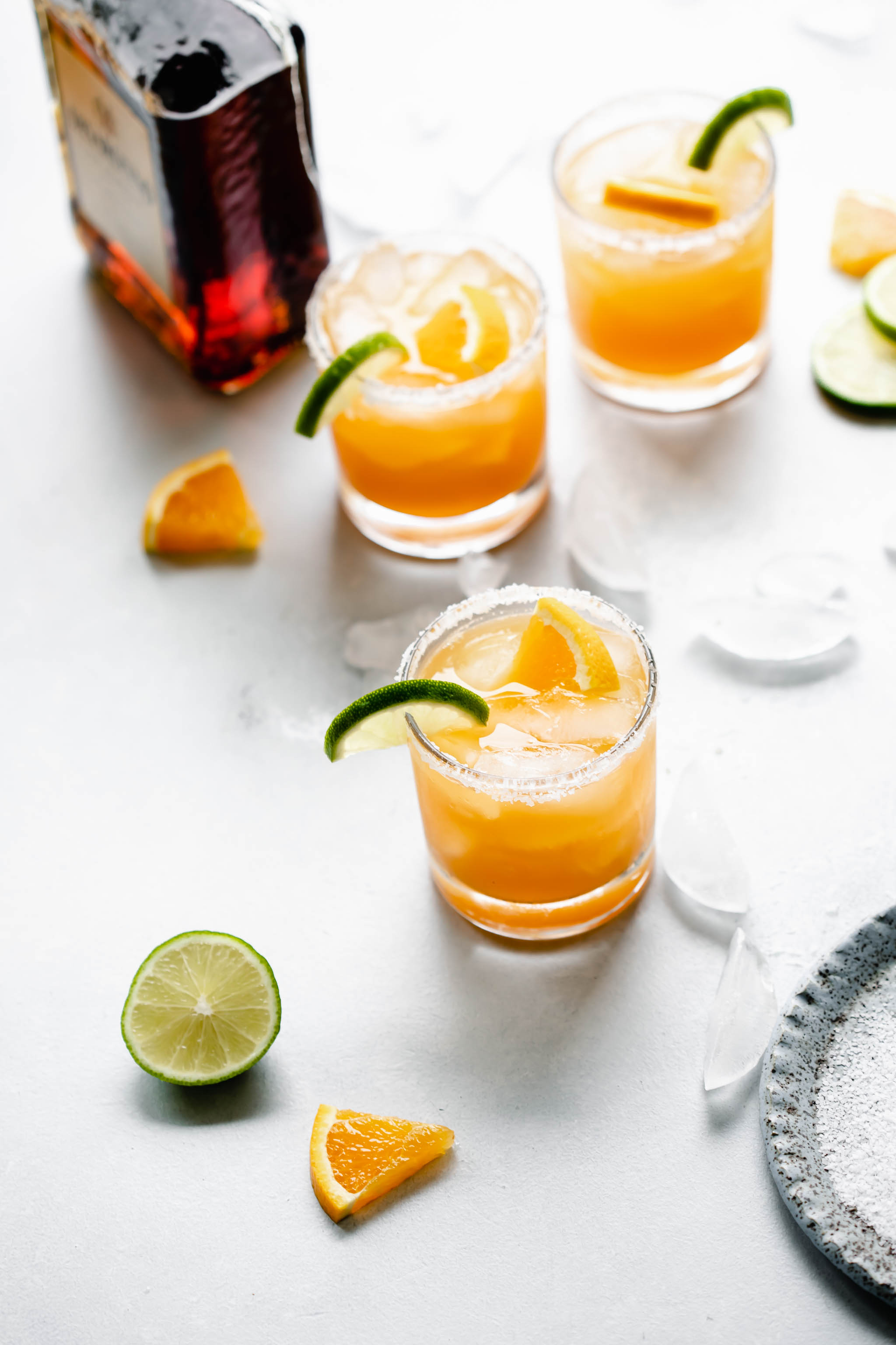 Three glasses of Italian Margarita rimmed with salt and garnished with orange and lime slices next to bottle of amaretto liqueur.