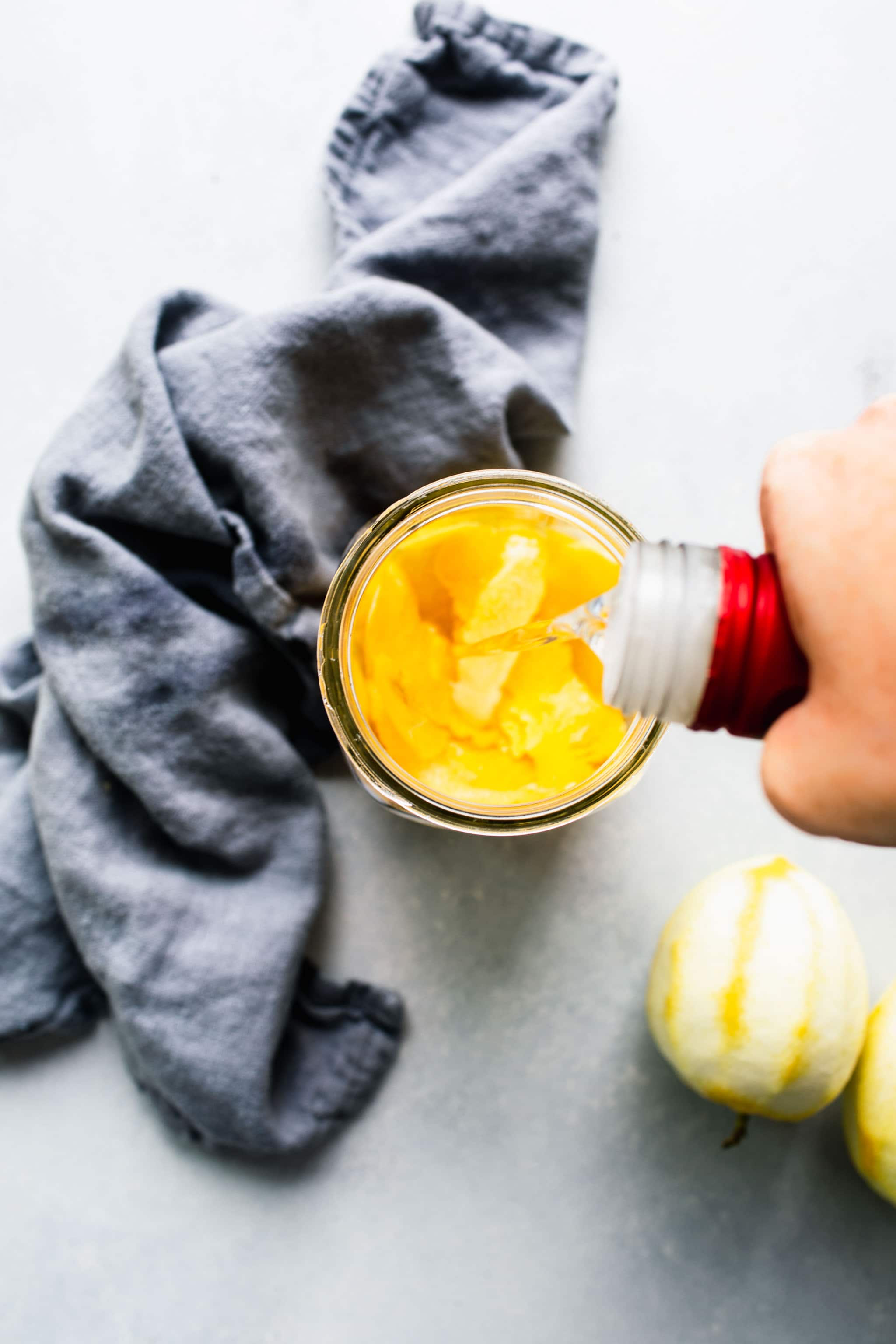 Vodka being added to mason jar with lemon peels.