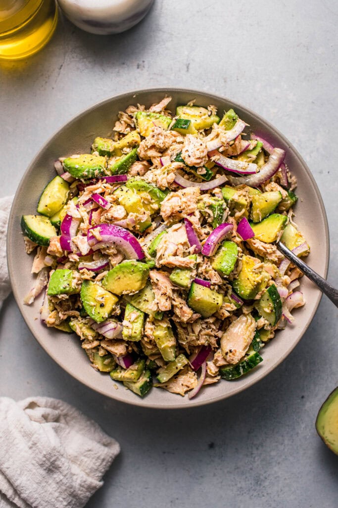 Overhead shot of cucumber avocado tuna salad in white bowl with serving spoon.