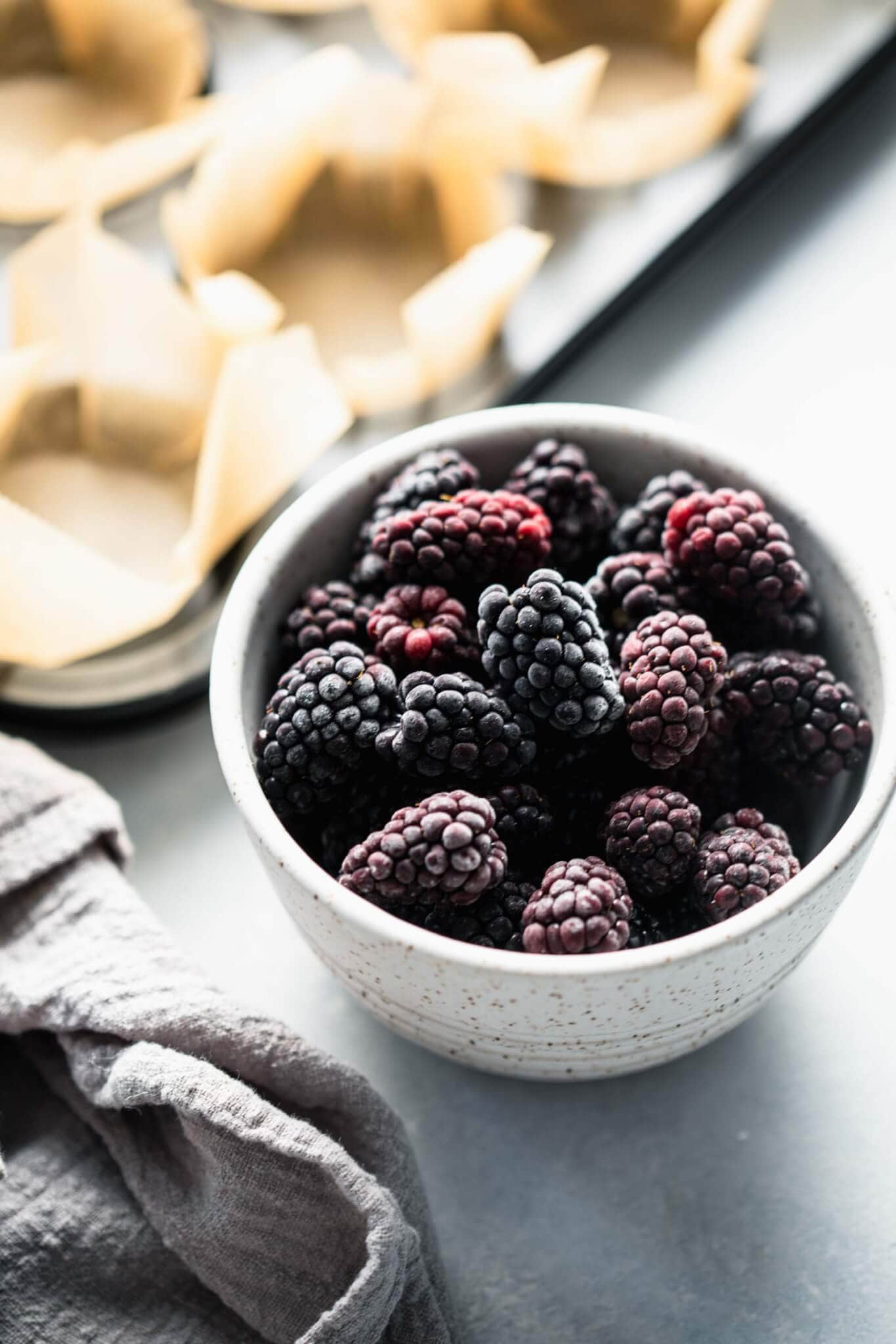 Bowl of frozen blackberries next to muffin tin.