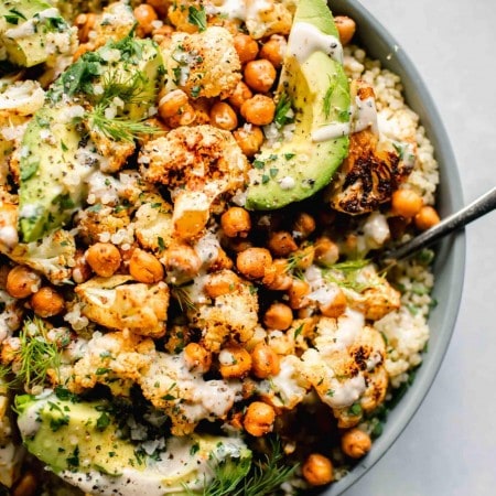 Overhead shot of roasted cauliflower salad in grey bowl with spoon next to small bowl of tahini dressing.