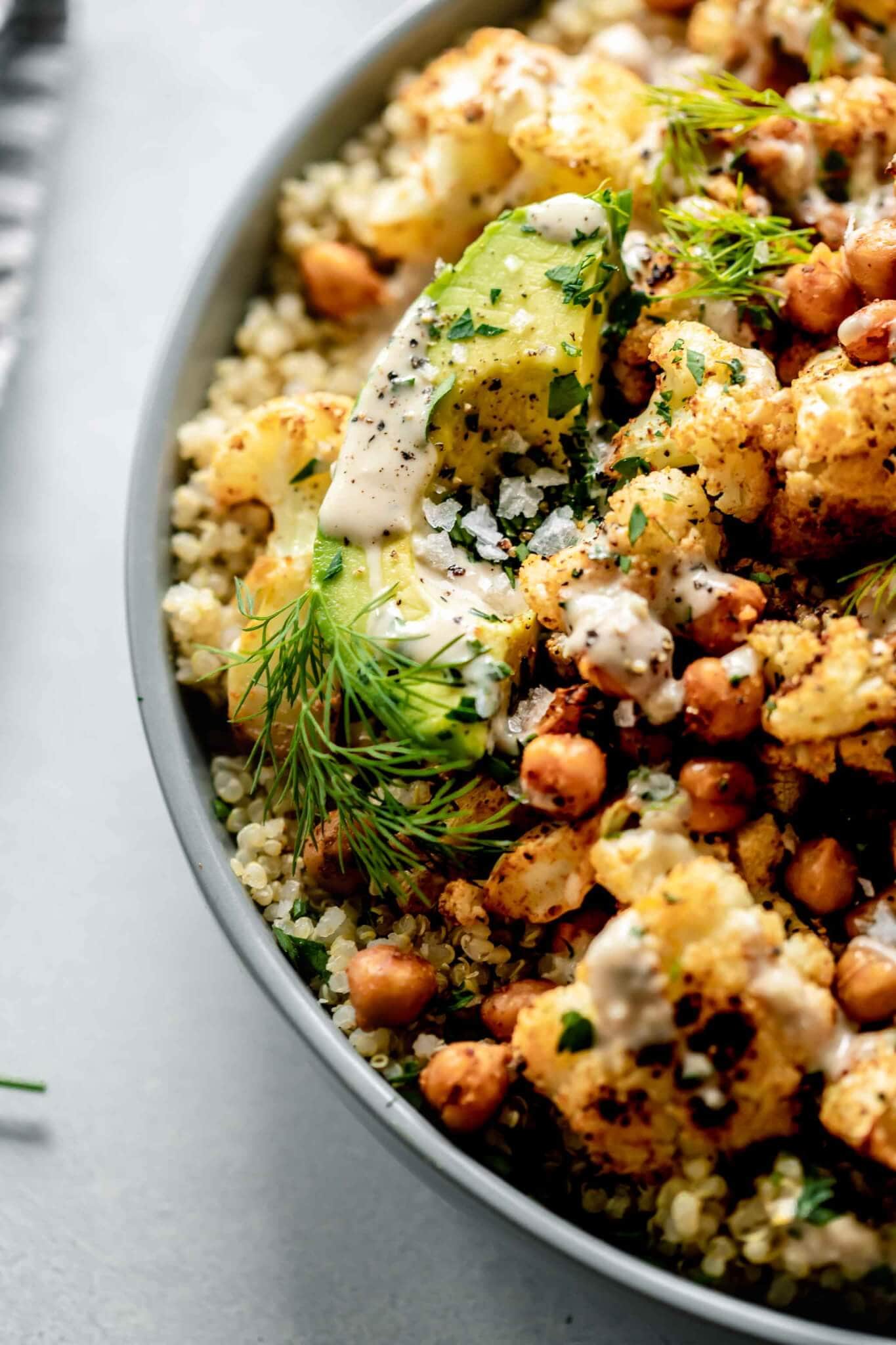 Overhead close up of bowl of quinoa salad in grey bowl with spoon topped with avocado.