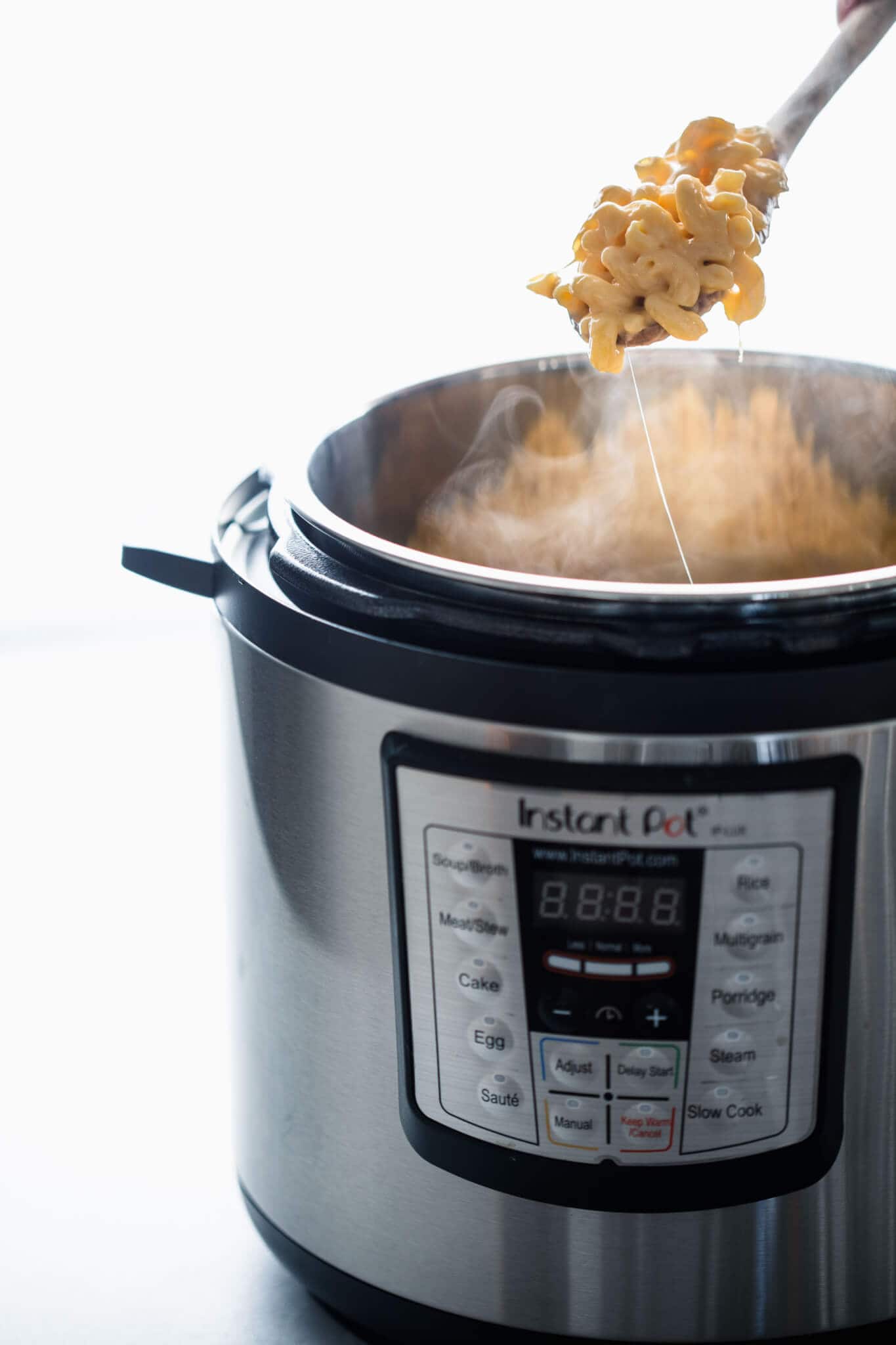 Side view of spoon pulling mac and cheese out of instant pot.