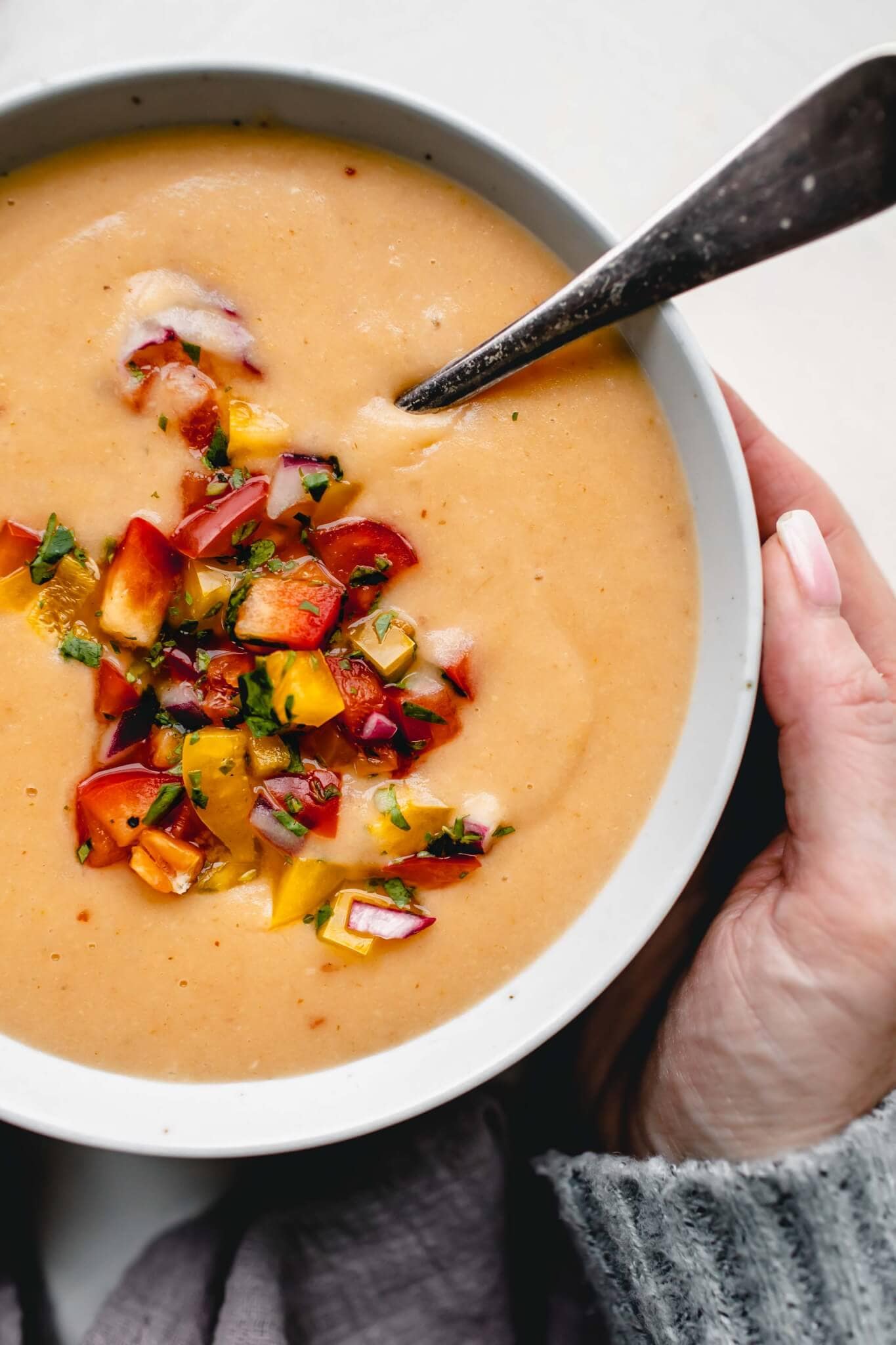 Hand holding bowl of potato cheese soup. 