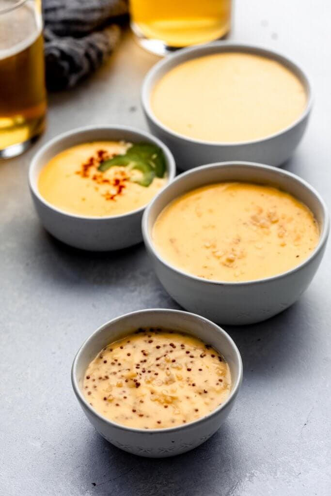 Side view of four bowls of cheese sauce next to two beers in glasses.