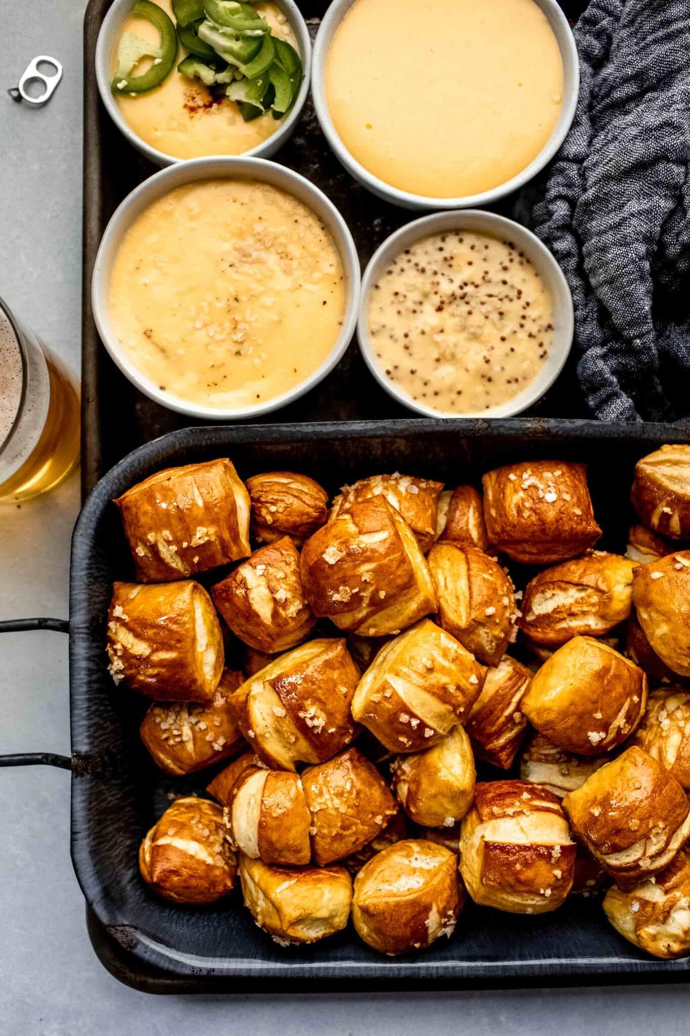 Overhead shot of pretzel bites on serving tray next to four types of cheese sauce.