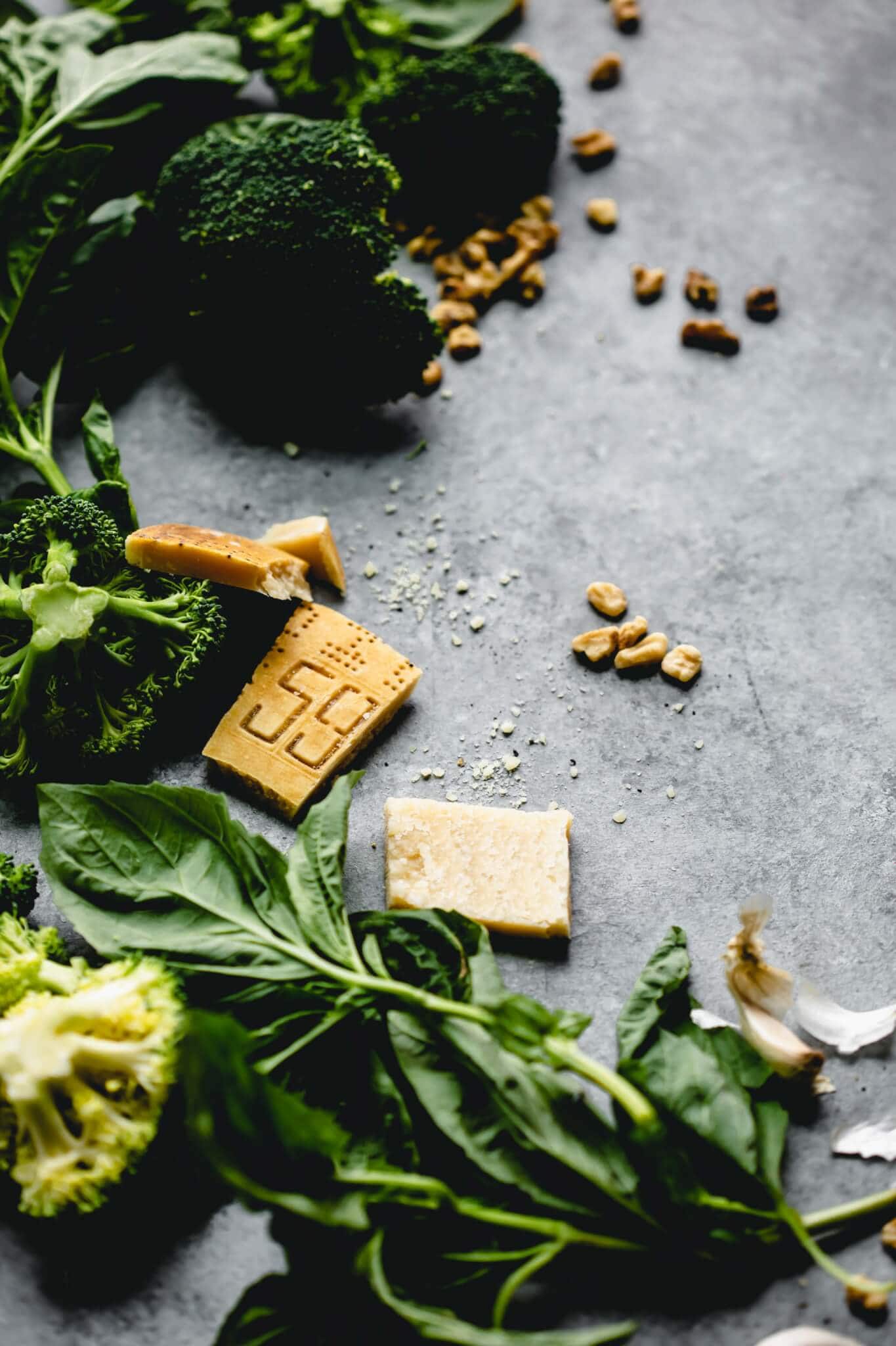 Ingredients for broccoli pesto laid out on concrete background.