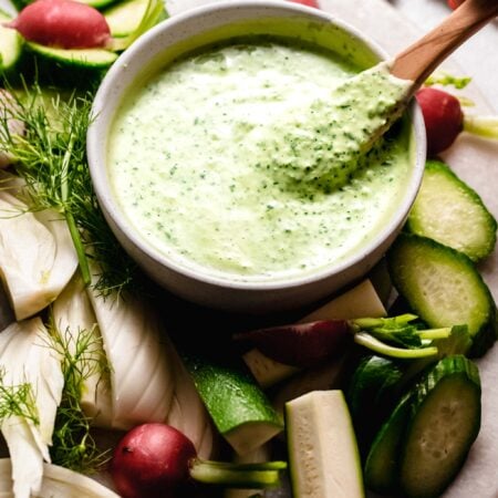 Hand holding spoon dipping into green goddess dressing.