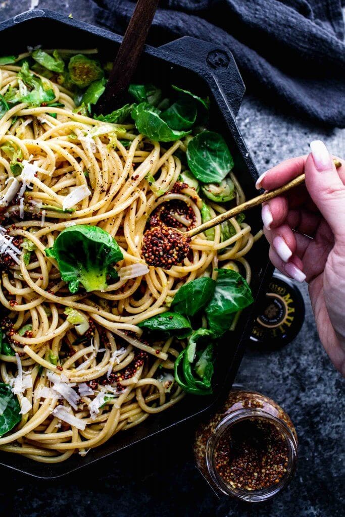 Hand dolloping mustard onto brussels sprouts pasta.