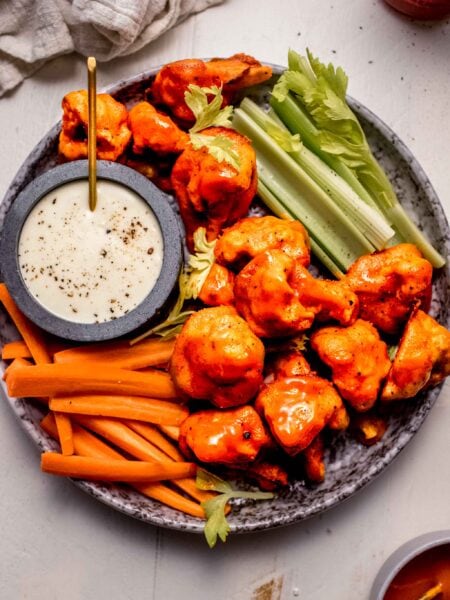 Buffalo cauliflower bites on plate with celery and carrot sticks and blue cheese dressing.