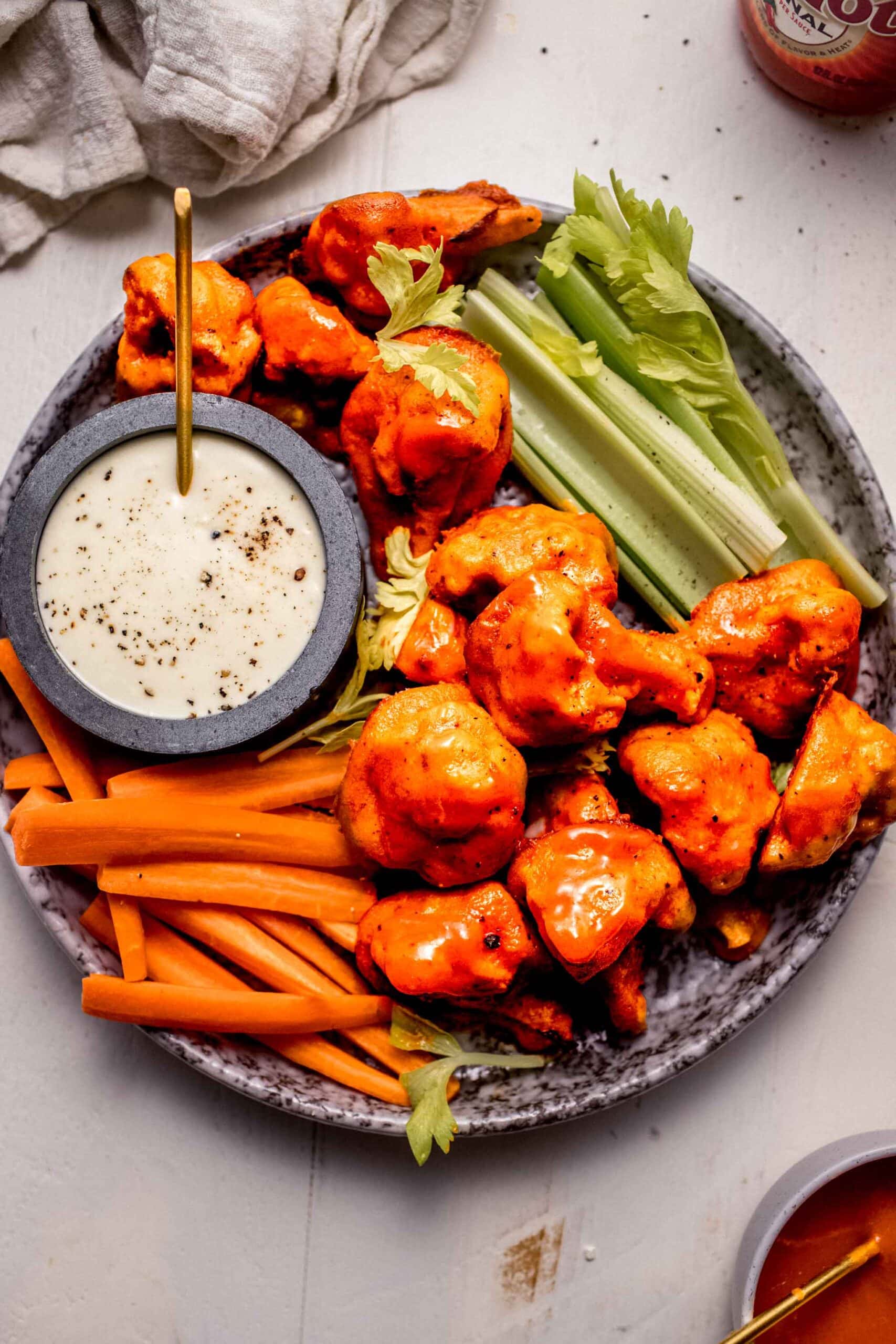 Buffalo cauliflower bites on plate with celery and carrot sticks and blue cheese dressing.