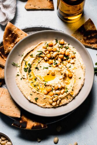 Hummus in bowl topped with macadamia nuts and parsley.