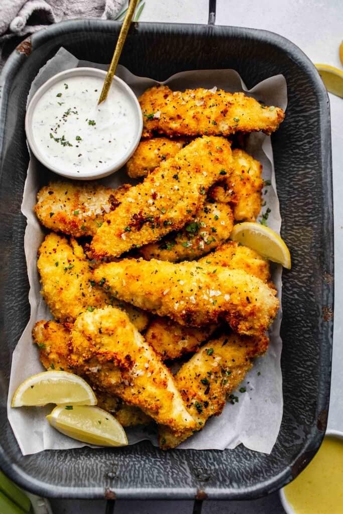 Air fried chicken tenders on serving tray with small bowl of ranch and lemon wedges.