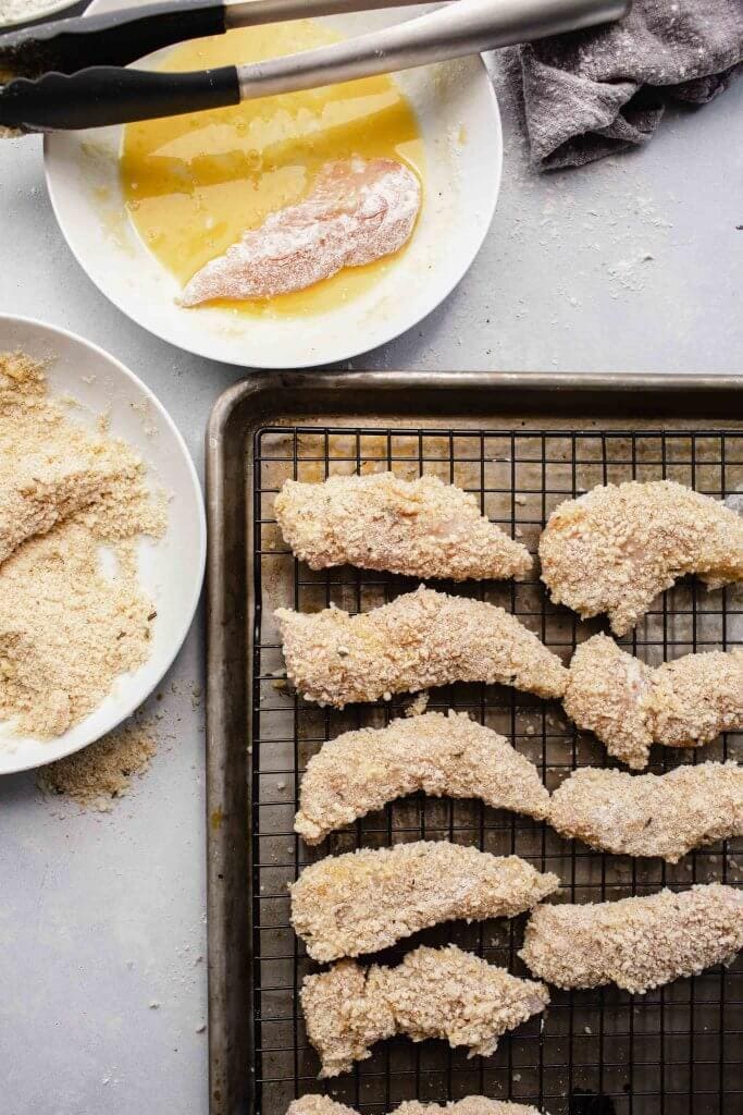 Breaded chicken strips on cookie rack before air frying.