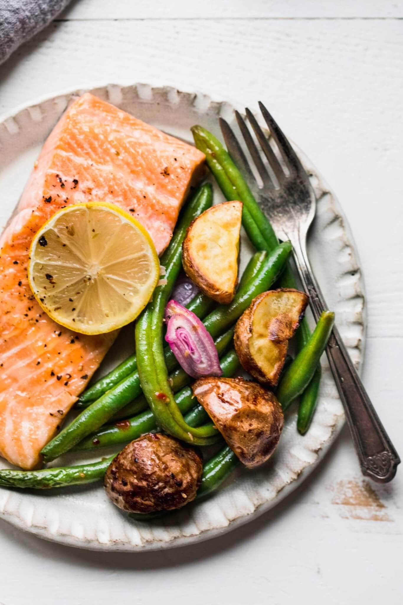 Salmon on plate with lemon slice, green beans and potatoes. 