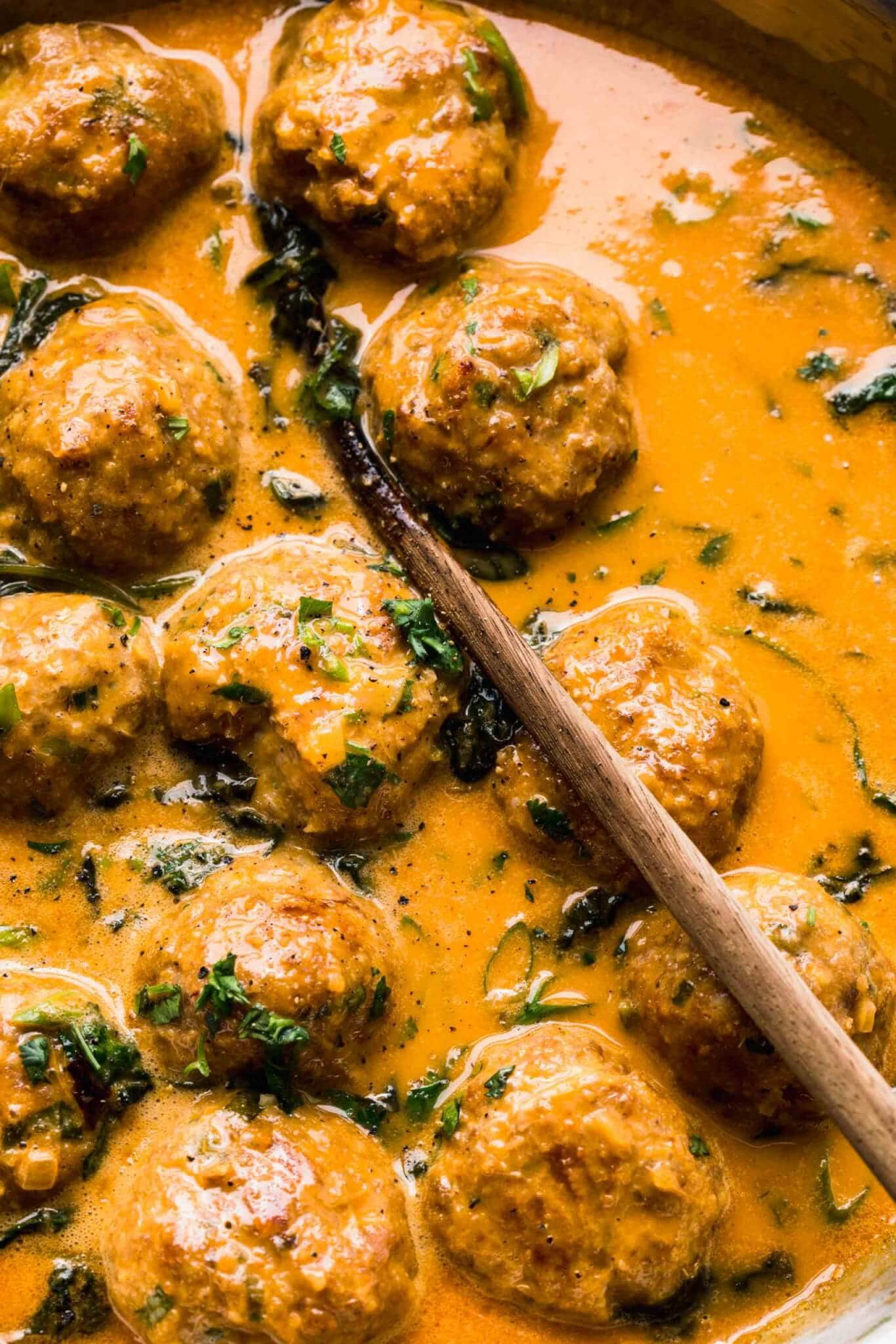 Meatballs simmering in curry sauce in skillet.
