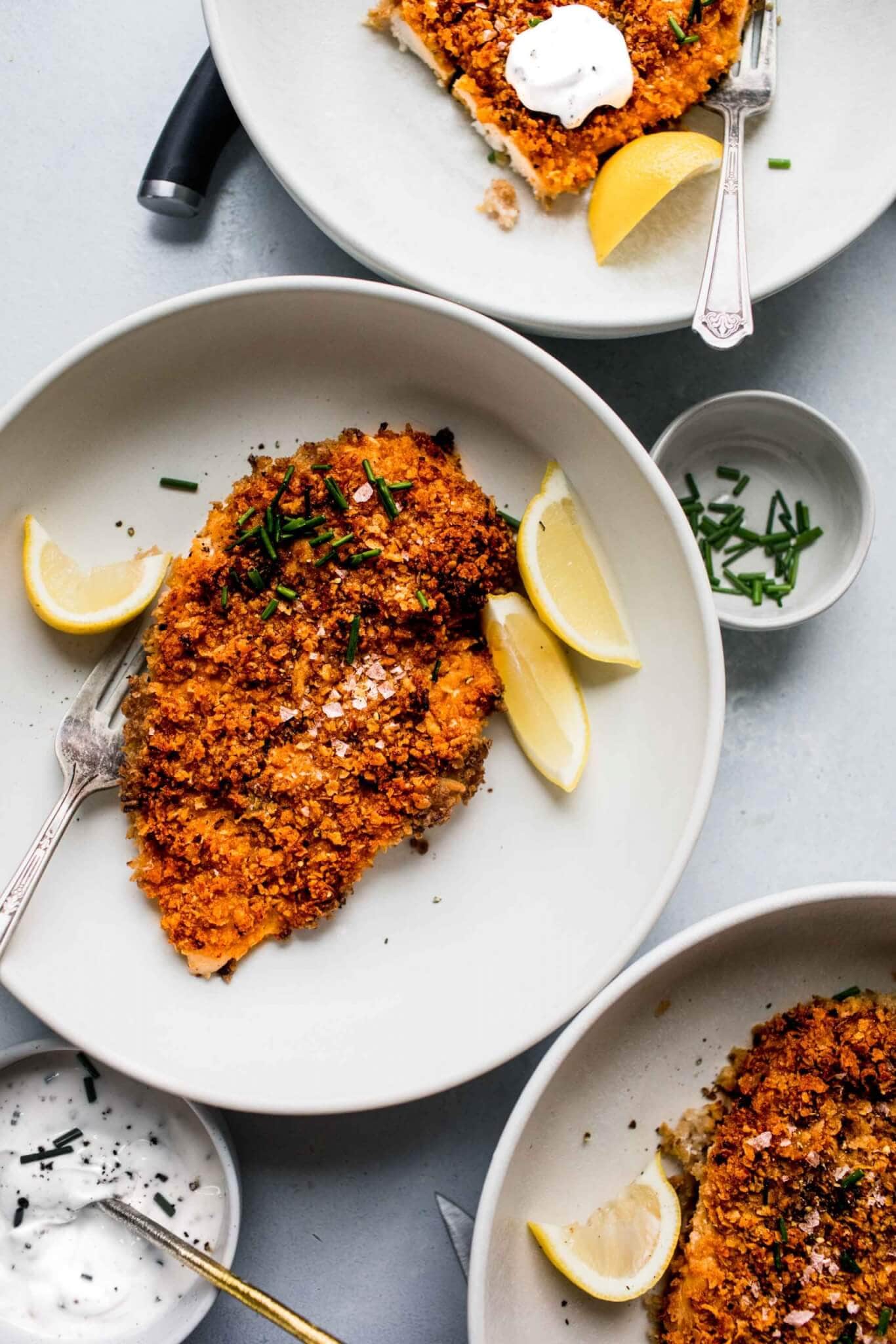 Three plates of crispy baked chicken served with chives, sour cream and lemon wedges.