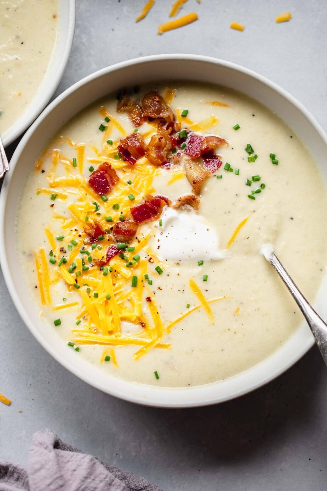 Overhead shot of bowl of cauliflower soup topped with dollop of sour cream, bacon and cheese.