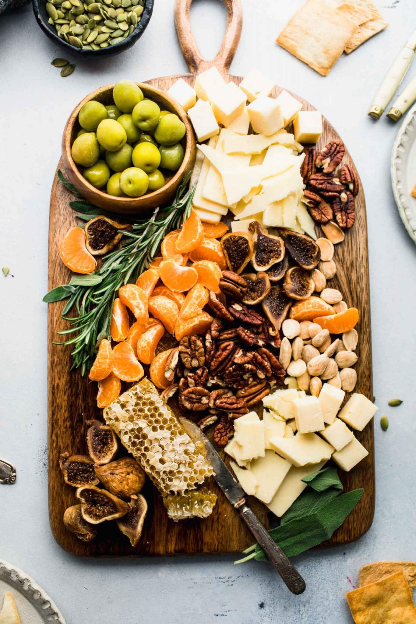 Cheeses, nuts, olives and fruits arranged on wooden serving board.