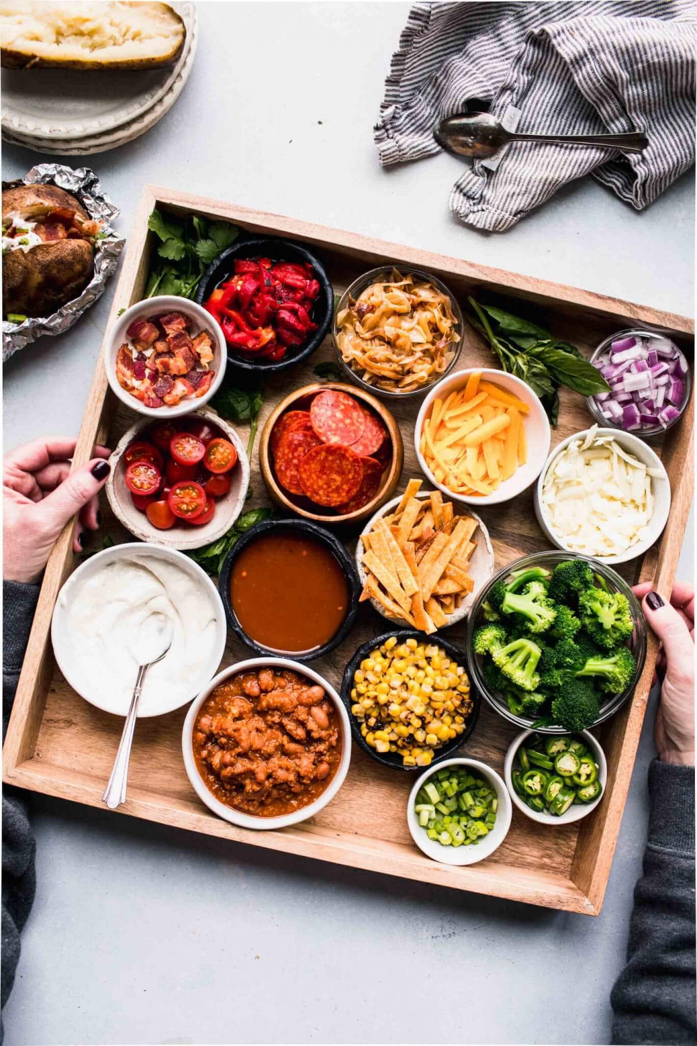 Wooden tray with toppings for baked potatoes on counter. 