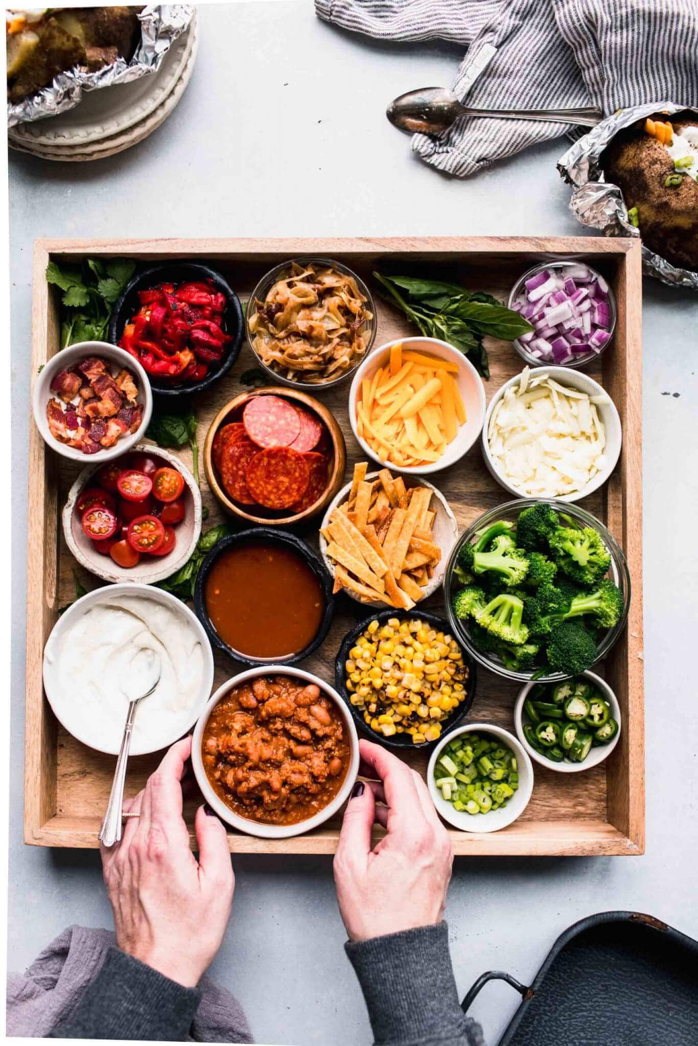 Hands arranging toppings for baked potatoes.