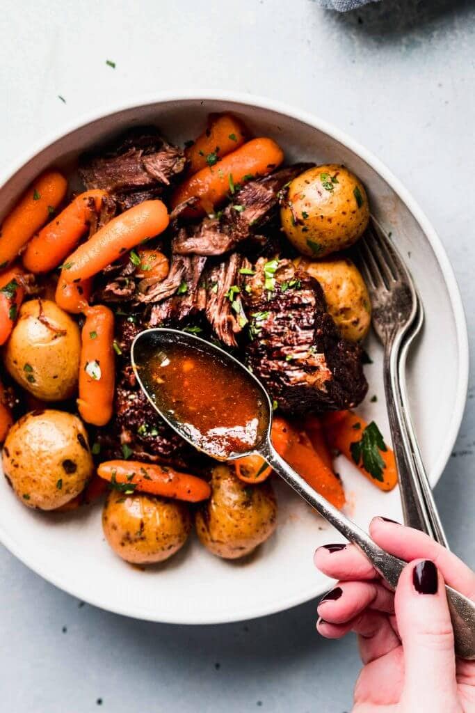 Sauce being poured onto pot roast in bowl.