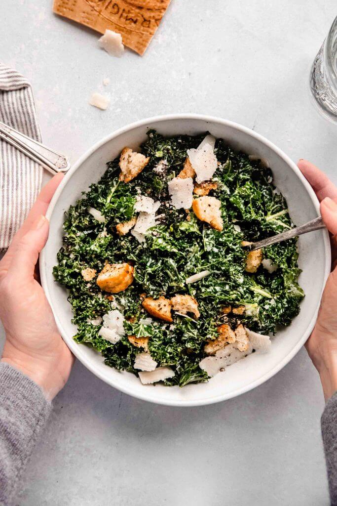Two hands holding bowl of caesar salad.