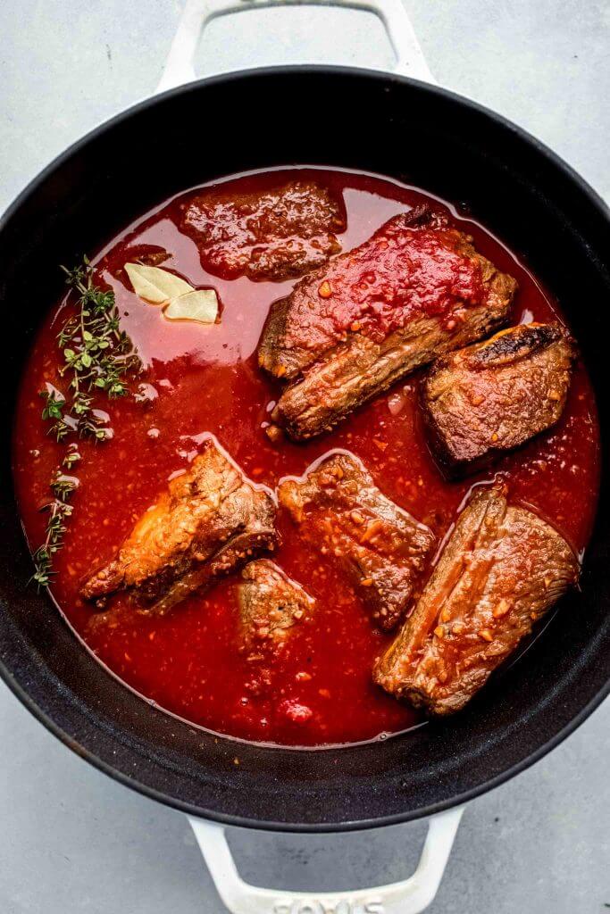 top shot of meat cooking in red sauce in dutch oven