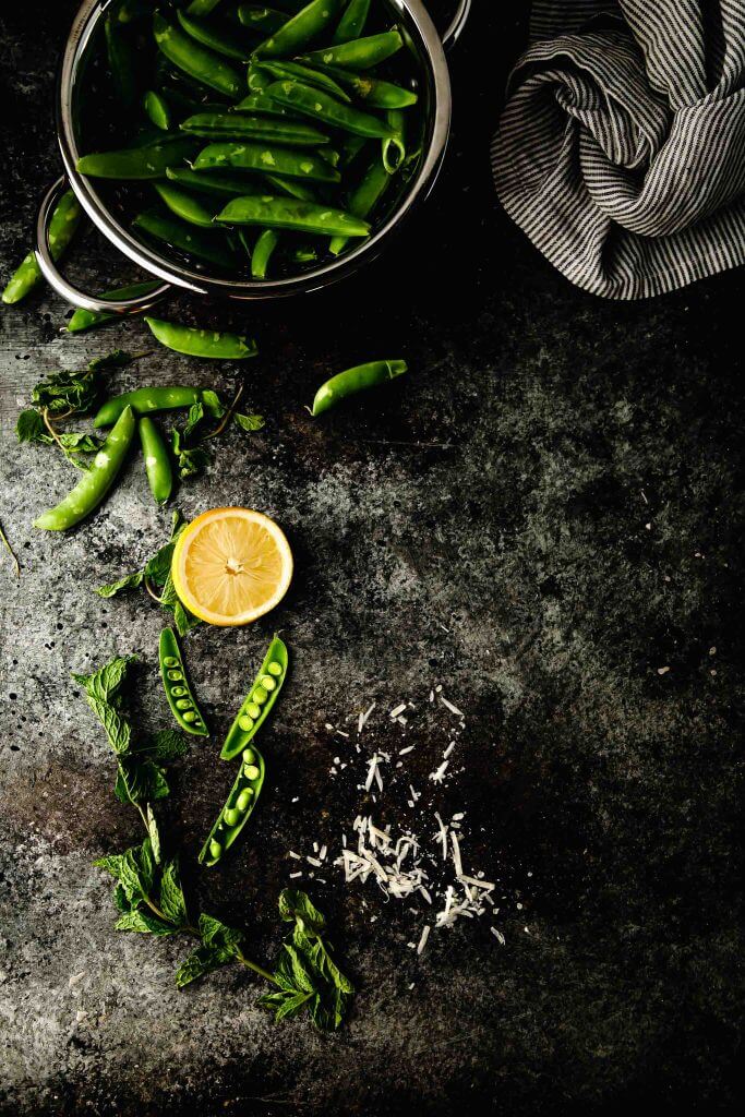 Peas, parmesan and lemon on dark grey counter.
