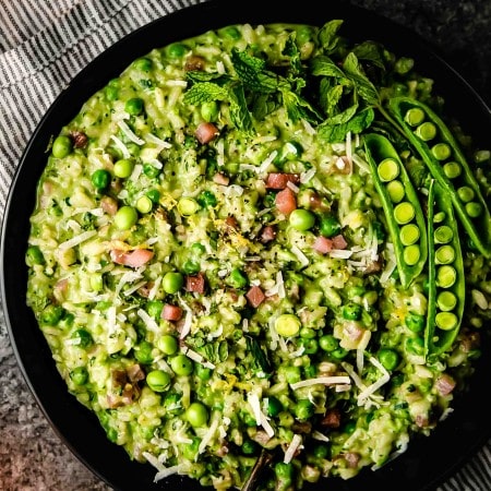 Pea risotto in black bowl with serving spoon.