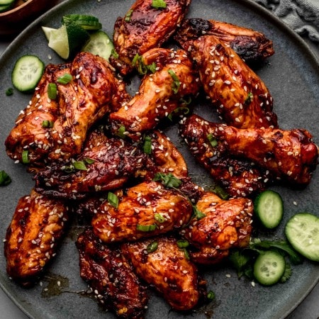 Wings arranged on grey plate scattered with cucumbers.